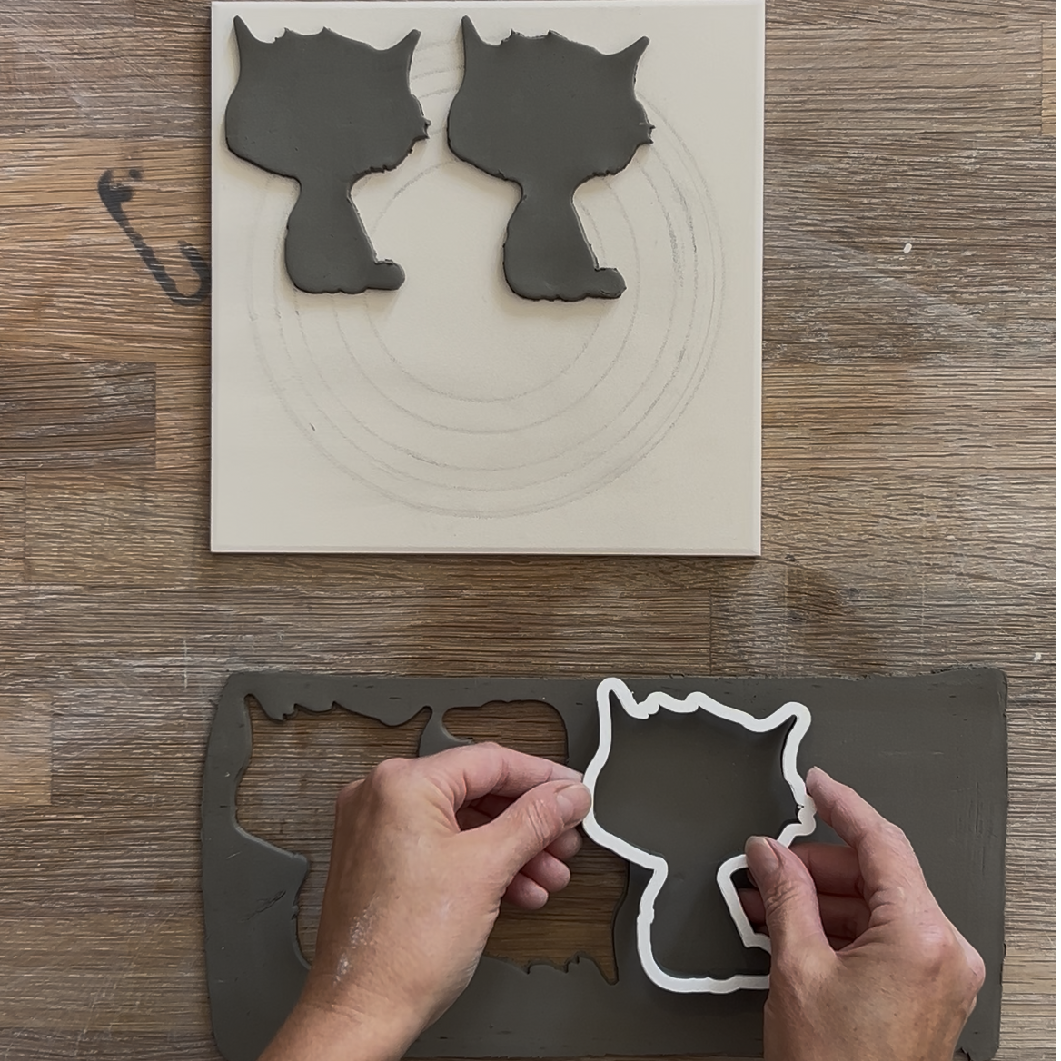 Ausstechen von Katzen-Formen aus einer grauen Tonmasse mit einer Konturen-Ausstechform für Halloween-Keramikprojekte auf einem Holztisch.