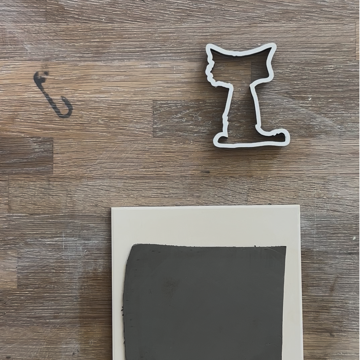 Ausstechen von Katzen-Formen aus einer grauen Tonmasse mit einer Konturen-Ausstechform für Halloween-Keramikprojekte auf einem Holztisch.