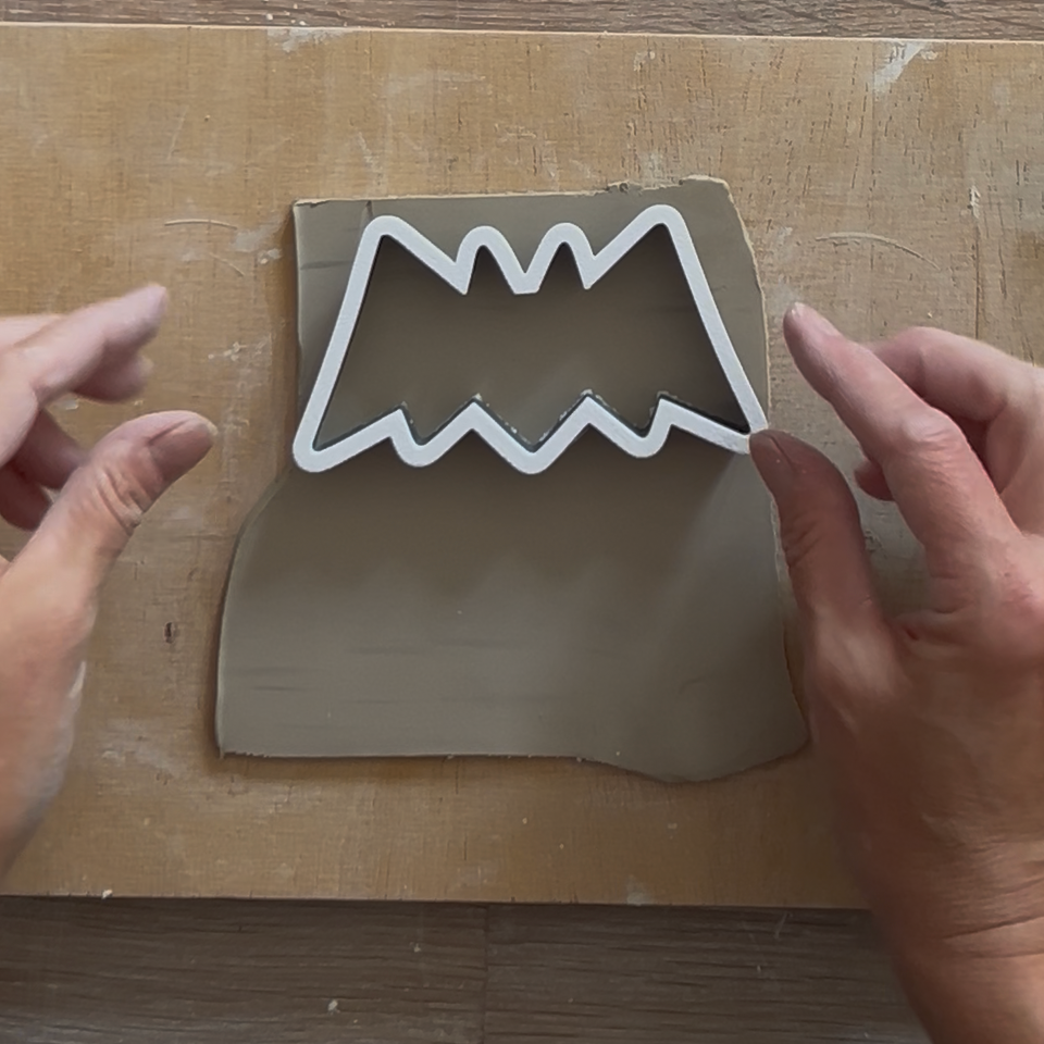 Anwendung einer Ton Ausstechform in Fledermaus-Optik. Kreatives Arbeiten mit einem Ausstecher fürs Töpfern von Halloween-Dekorationen aus Ton auf einem Holzbrett.